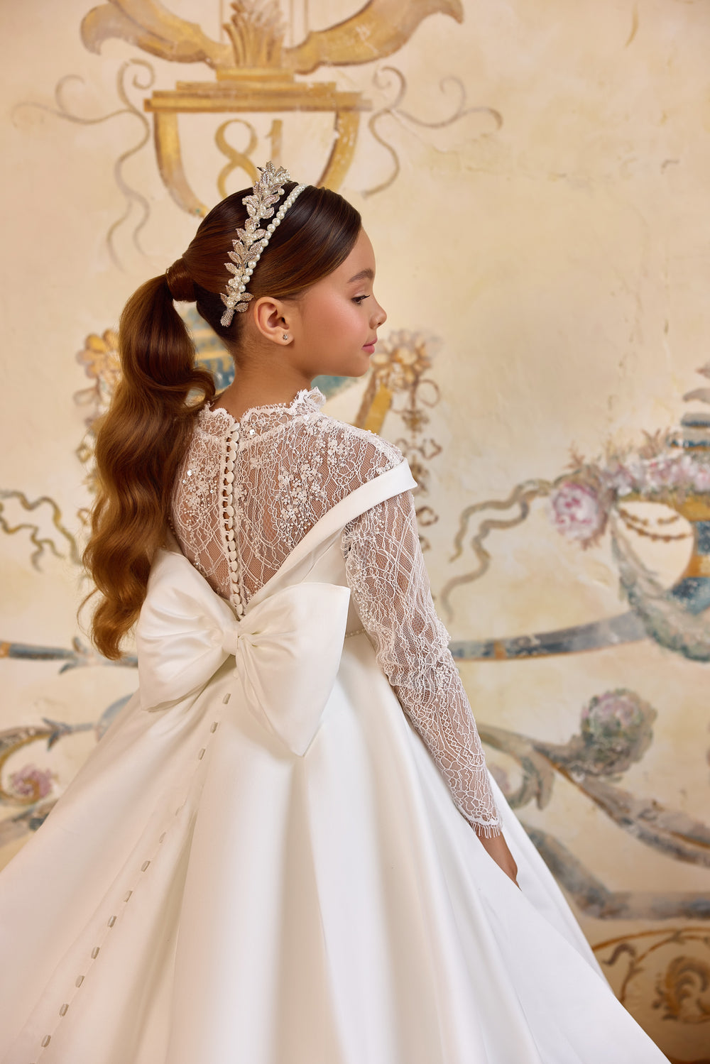 Gabriela luxury First Communion gown with illusion lace bodice, off-the-shoulder neckline, oversized bow, and cathedral-length satin train.