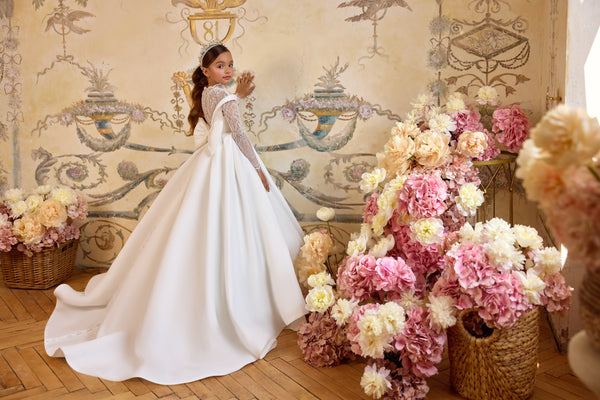 Gabriela luxury First Communion gown with illusion lace bodice, off-the-shoulder neckline, oversized bow, and cathedral-length satin train.